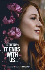 It Ends With Us 4 Book cover for "It Ends With Us" by Colleen Hoover. The cover features a photograph of a woman with long red hair smiling softly, facing right. Pink flowers are scattered across the image. Text at the bottom states the book is now a major motion picture.